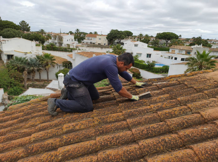 Trabalhador a limpar telhas de um telhado em Faro com uma escova